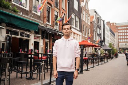 COC jongere Huib staan in de regulierdwarsstraat met regenboogvlaggen.