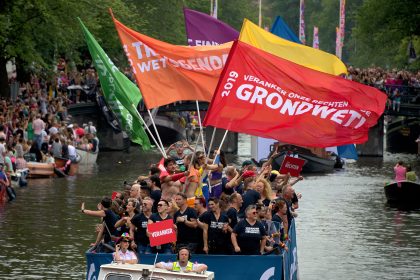 COC voerde succesvol actie voor verankering van LHBTI+ rechten in de Grondwet. We zien mensen in een boot met verschillende vlaggen in de kleuren van de regenboog met teksten over de grondwet – foto Tom Knoflook
